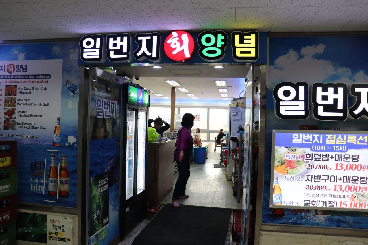 Entrada de la Casa de Pescado Ilbeonji en el Mercado de Pescado de Noryangjin, con cartelines luminosos.